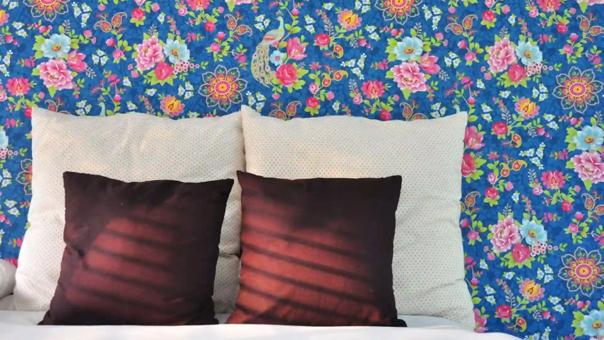 Bedroom with vivid blue floral wallpaper, white bedding and deep burgundy accent pillows.